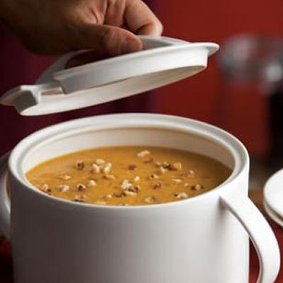 A pot of roasted pumpkin and apple soup with a hand removing the lid.