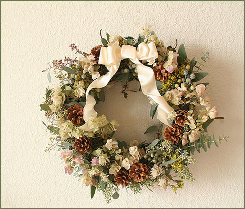 Subtle Christmas wreath decorated with pine cones, a white ribbon, and white flowers.