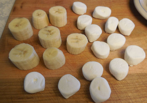 Bananas and marshmallows on a cutting board.