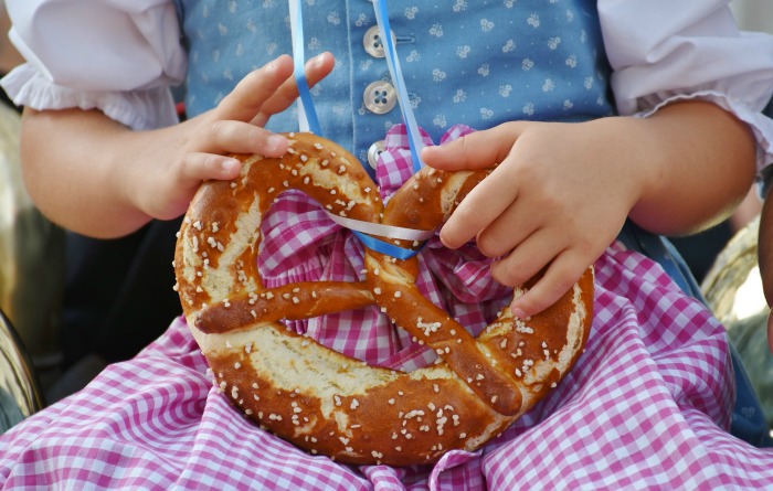 A girl with a large pretzel. A little girl wearing a checked skirt and blue and white blouse holding a Bavarian pretzel.