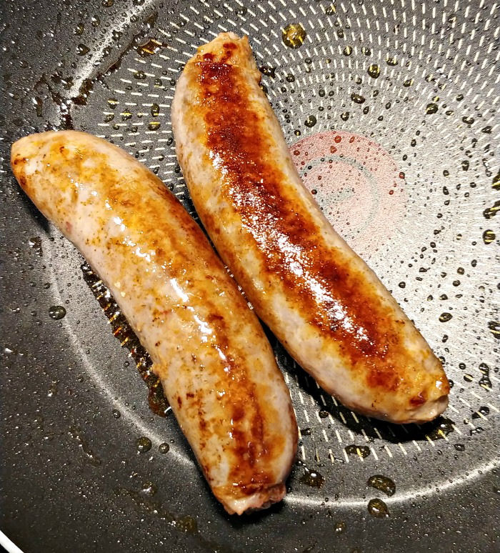 cooking Italian sausages Two sausages in a non stick pan.
