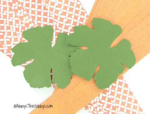 Paper pumpkin supplies, including green scrapbook paper cut into leaf shapes, and strips of orange scrapbook paper to make the body of the pumpkin.