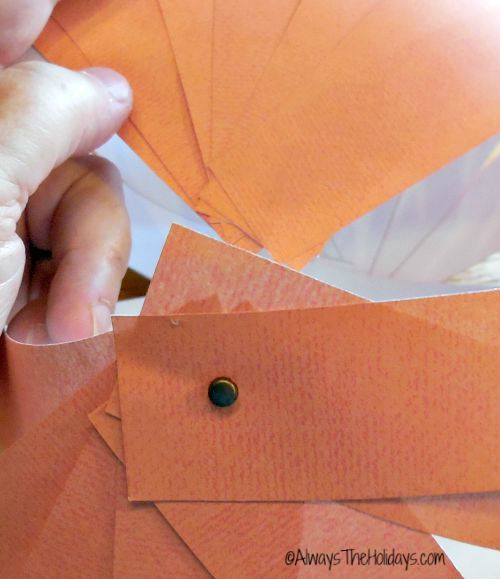 A close up photo of the top of a paper pumpkin craft where scrapbook paper is attached with a small brad.