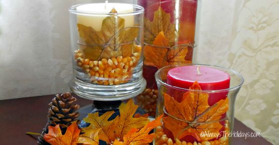 Popcorn table decorations Three hurricane popcorn table decorations on a table with leaves and pinecones around them.