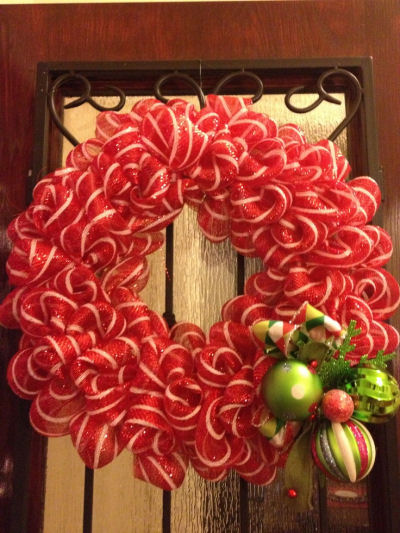 A red and white wire rimmed ribbon wreath hanging on a door.