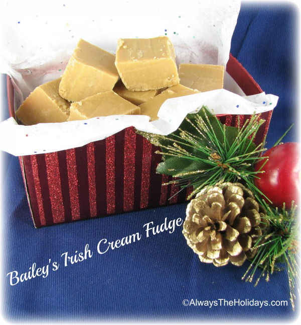 Bailey's Irish cream fudge in a red striped box on top of a blue tablecloth next to a pinecone on a bine bough.