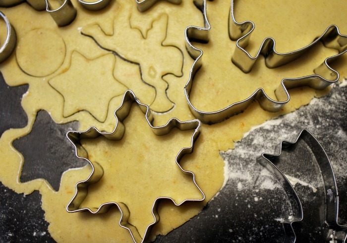 Making Christmas cookies with cookie cutters. Christmas themed cookie cutters cutting shapes into cookie dough on a floured counter.