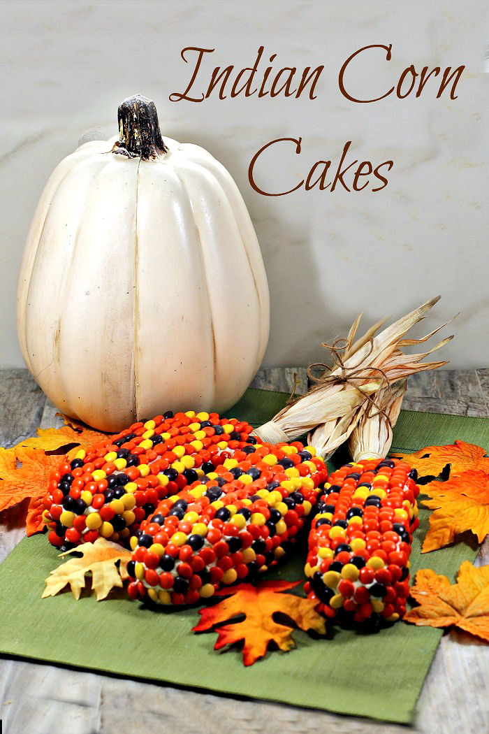 Display of Indian corn cakes with pumpkins and leaves. Display of pumpkins, leaves and colorful cakes with text reading "Indian corn cakes."