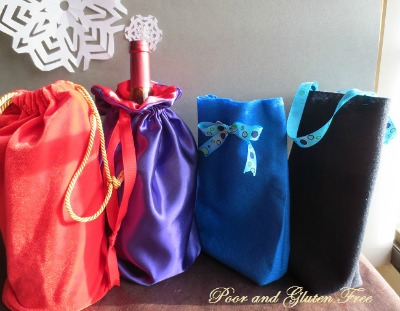 Four drawstring Christmas gift bags, in red, purple, blue and black.