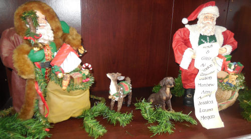 Two detailed Santa figures, one holding a sack of presents and a walking stick, the other holding a sack of presents and a list of names.