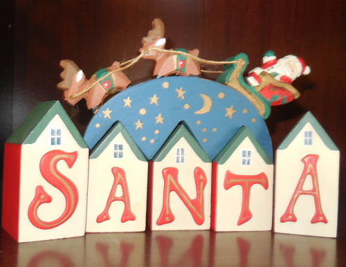 Midwest Santa block letters, with a Santa being pulled by a sleigh of two reindeer riding over the letters.