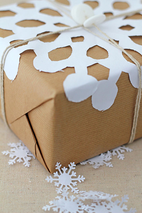 Snowflake gift wrap project on a brown paper present with paper snowflakes scattered around it.