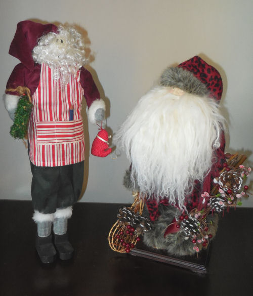 Two traditional style Santa Claus figures. Traditional Santa Claus figures, one standing holding a bird, and one in a sleigh of pinecones.
