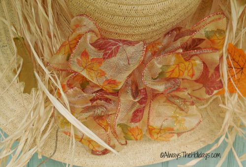 A fall bow tie made from a 1 1/2 inch wire ribbon with a fall pattern, attached to a straw hat which is the base for a straw hat door decoration.