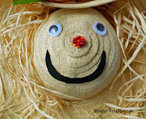 A close up image of a straw hat scarecrow wreath, focusing on its eyes, nose and mouth, with some of its raffia hair poking out around it's face.