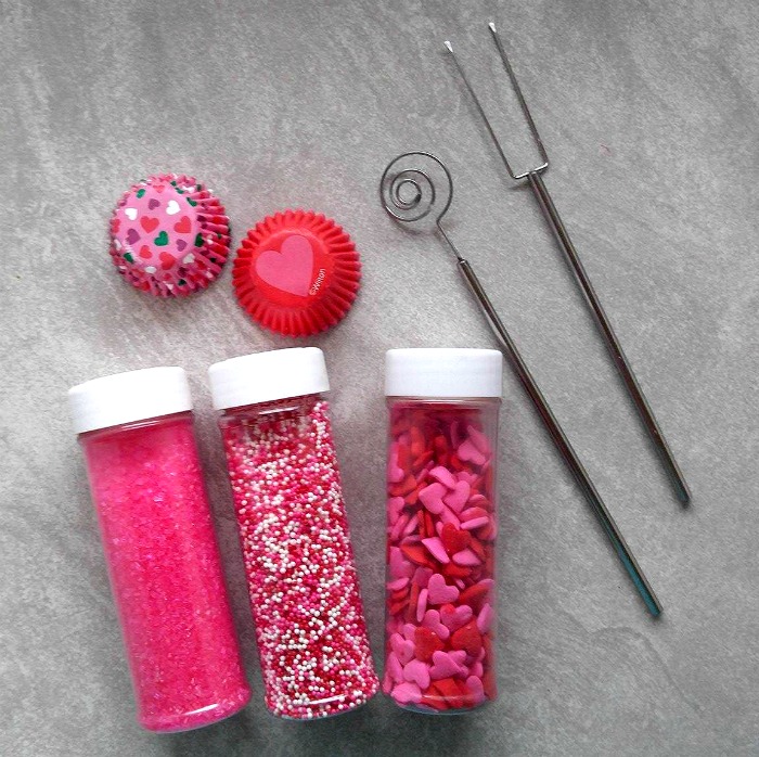 Sprinkles and dipping tools for my raspberry cheesecake truffles on a grey marble board.