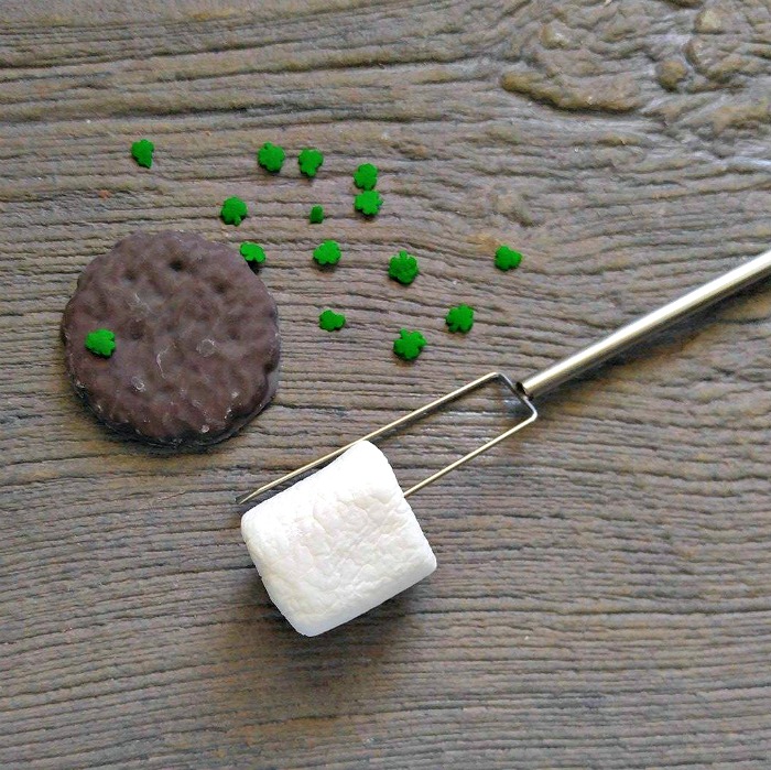 candy dipping tool Girl scout cookie with shamrock sprinkles and a marshmallow on a metal fork.