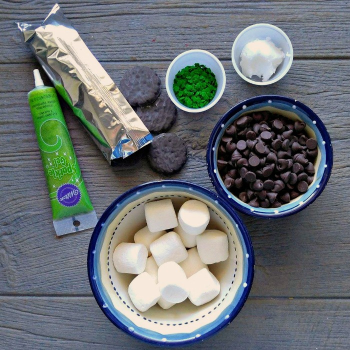Ingredients for the Leprechaun hats Girl Scout thin mints, shamrock sprinkles, coconut oil, green gel frosting, marshmallows and chocolate chips in bowls.