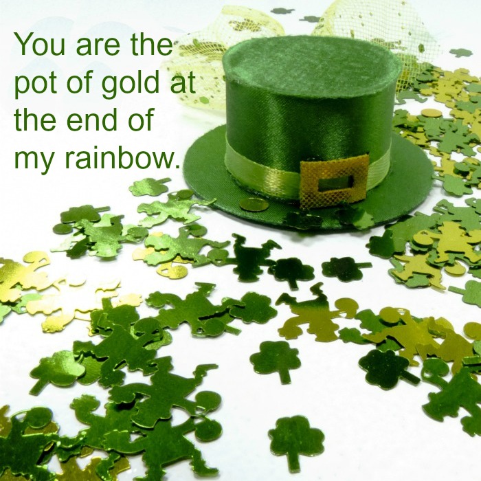 Pot of gold quote over a white table with a green hat and four leaf clovers on it. A green hat and fake shamrocks on a white table with a pot of gold quote text overlay.