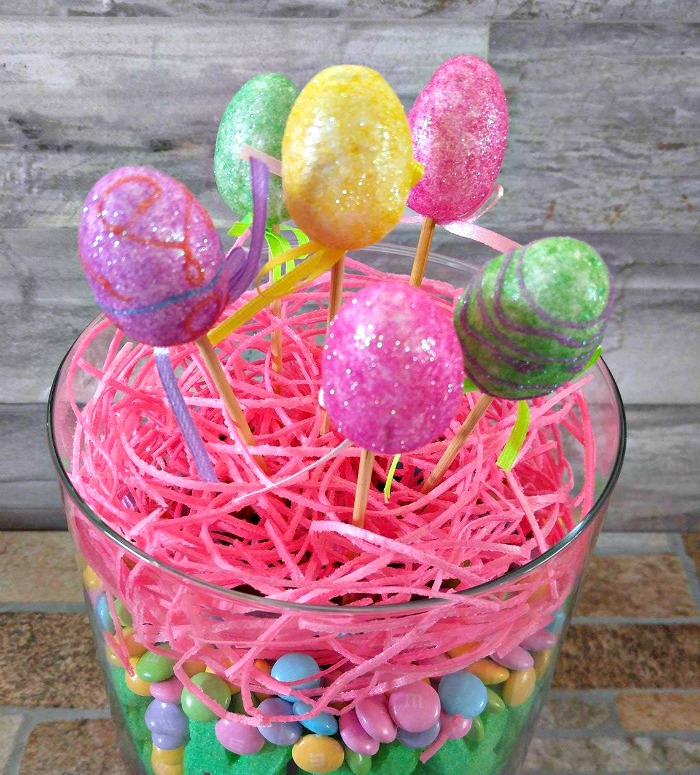 Easter Egg pins sitting in pink grass and candy in a clear vase. Add the foam Easter Egg picks