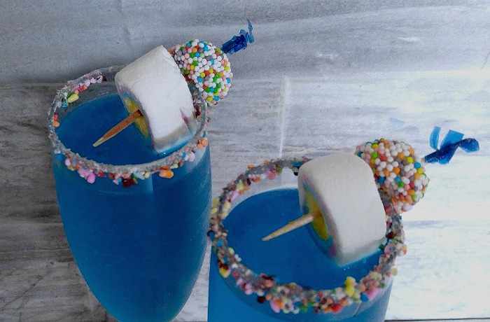 A marshmallow allsort garnish on a blue drink. Garnishing the glasses with sprinkles and a cocktail garnish made of marshmallows and licorice allsorts.