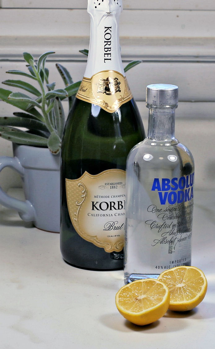 A bottle of vodka and champagne with lemons in front of it on a counter.