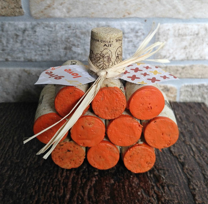 A mini wine cork pumpkin project with paper leaves and raffia sitting on a wooden tabletop.