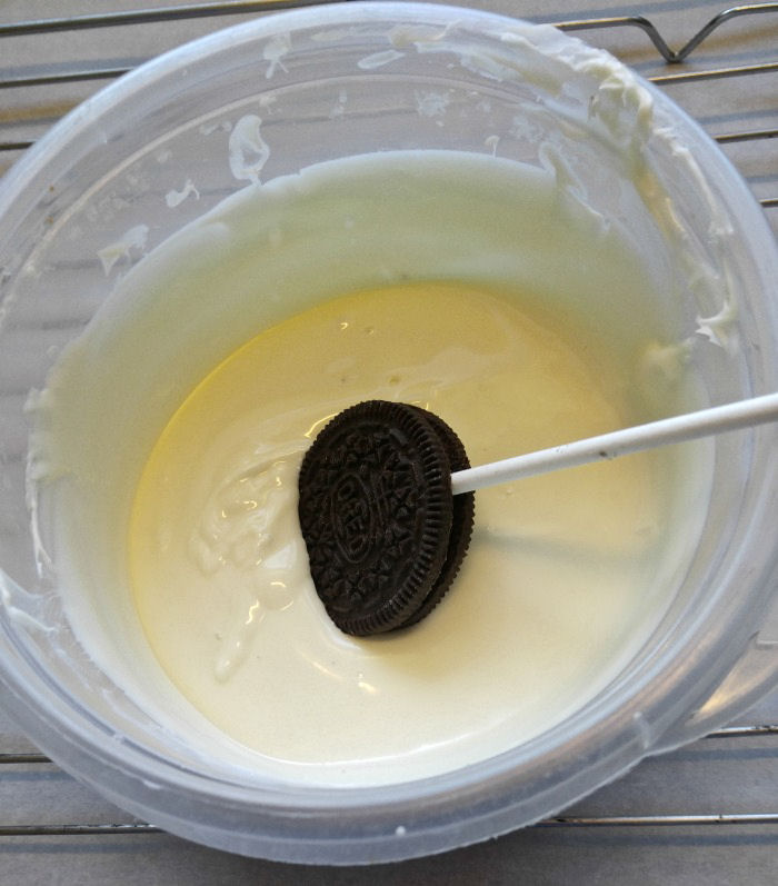 Dipping a cookie pop into melted white chocolate Dip the Oreo cookie in melted white chocolate