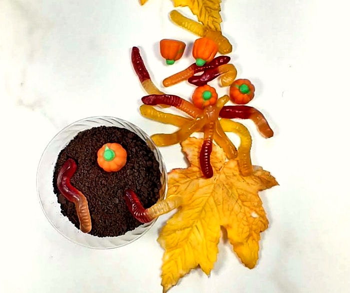 Dirt pudding cups with gummy worms, pumpkins and leaves. Gummy worms and candy pumpkin on a dirt pudding cup