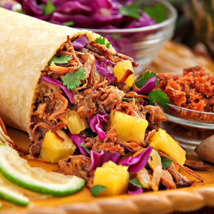 A stuffed Al Pastor burrito on a cutting board to celebrate National Burrito Day (the first Thursday in April).