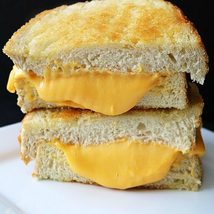 A grilled cheese sandwich cut in half stacked on top of each other, with yellow cheese oozing out.
