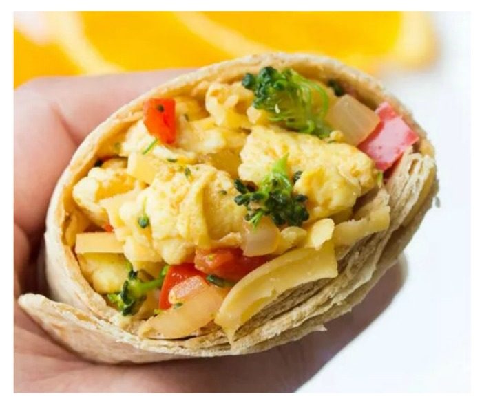 Breakfast burrito. A hand holding a breakfast burrito with red peppers and broccoli.