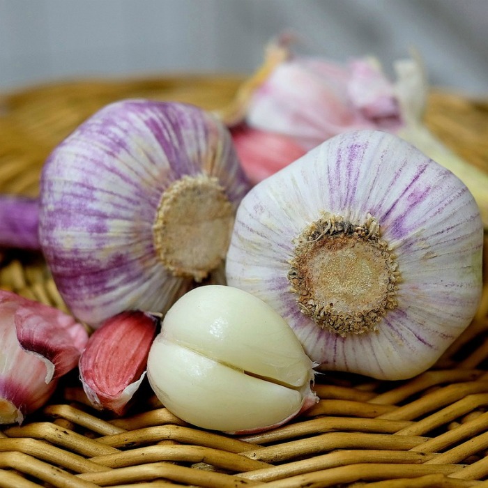 A clove of garlic, and three garlic bulbs on a wooden mat for National Garlic Day.