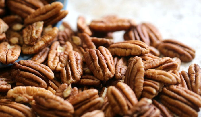 A pile of pecan nuts. A pile of pecan nuts spilling onto a counter.