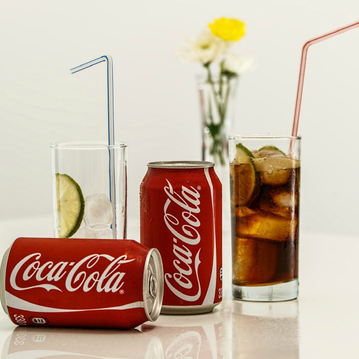 A glass of ice, and a glass of ice filled with Coke next to two Coca Cola cans.
