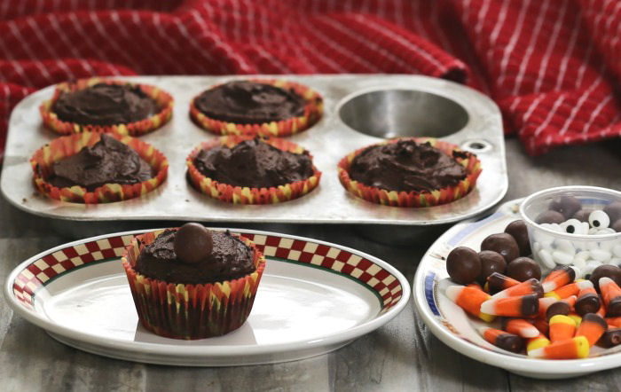 malted milk ball on a chocolate cupcake Cupcake on a plate with a malted milk ball near a tray of cupcakes and plate of candy.