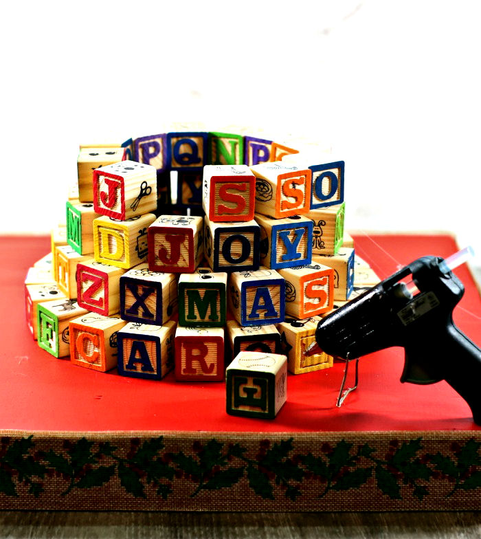 Building an alphabet block tree. Alphabet blocks in a circle and a glue gun on a red Christmas base.