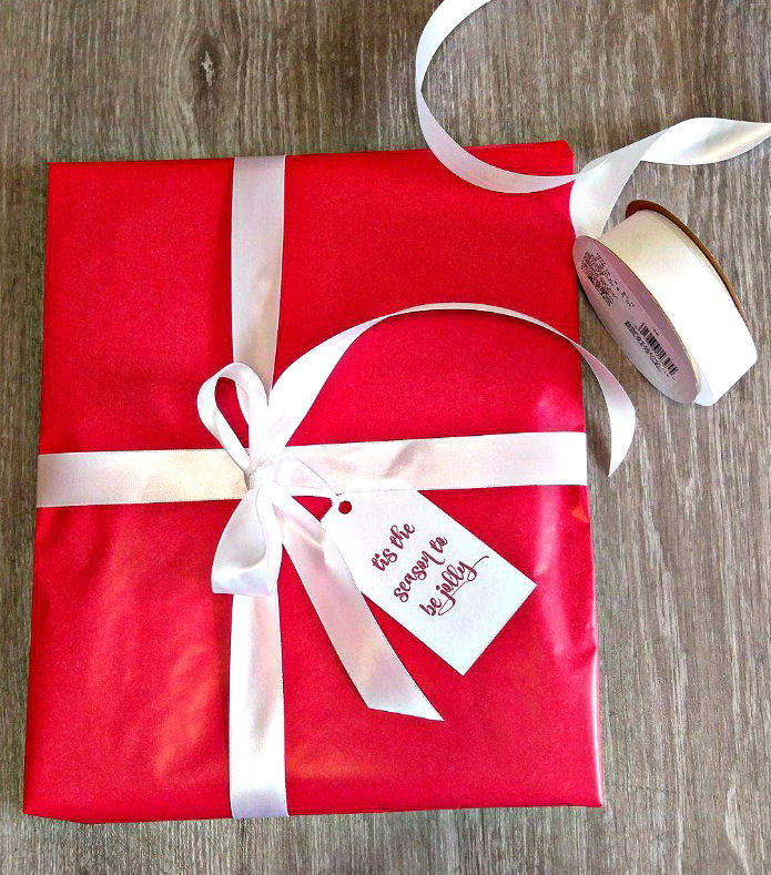 red and white gift with a message gift tag Red present with white ribbon and message gift tag reading "tis the season to be jolly."