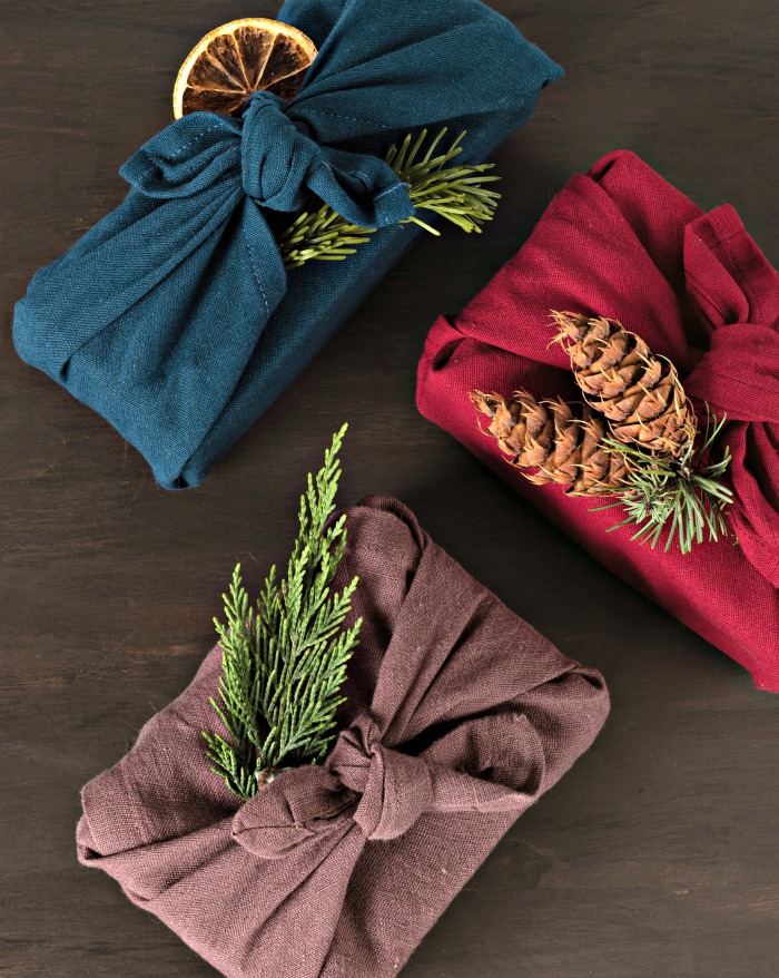 Books wrapped in clothing with greenery. Furoshiki gifts. Eco friendly alternative green Xmas presents wrapped in clothes with boughs, pine cones and dried orange slices.