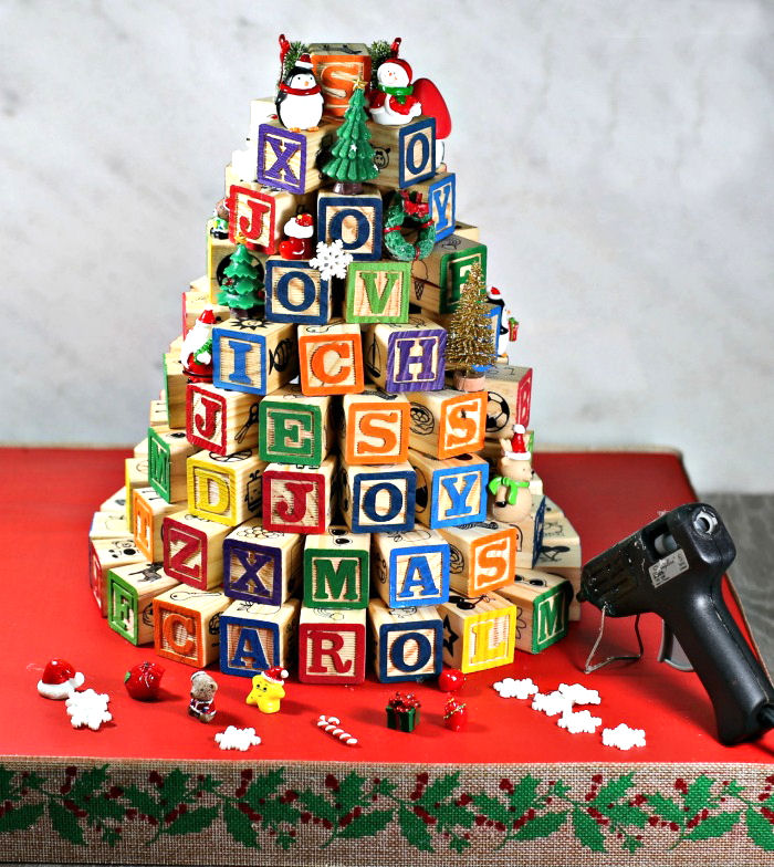 Building an alphabet block tree. alphabet block tree with glue gun and mini ornaments on a red base.