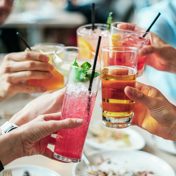 A group of five friends clinking cocktails over a brunch table.