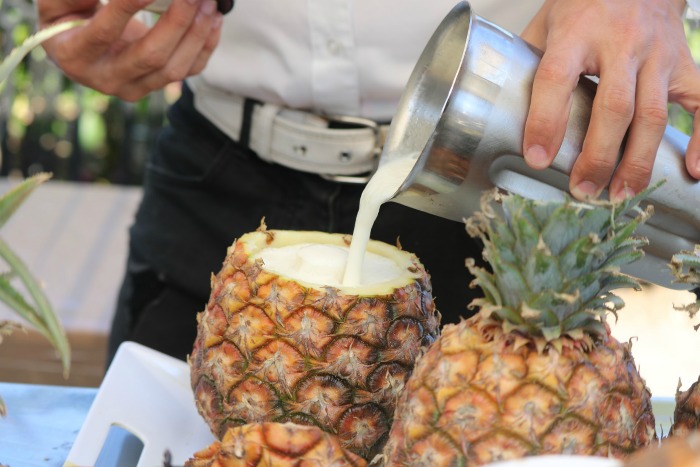 A blended pineapple cocktail in a pineapple. A bartender pouring a blended Pineapple cocktail into a hollowed out pineapple on National Cocktail Day.