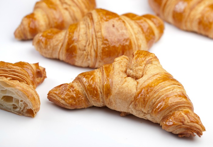 Croissants on a white countertop. Five croissants on a plain white counter, one of the croissants is cut in half.