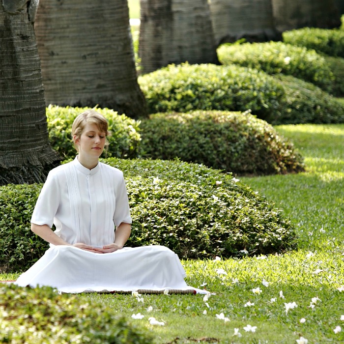 Woman in a white dress doing a seated meditation in a garden.