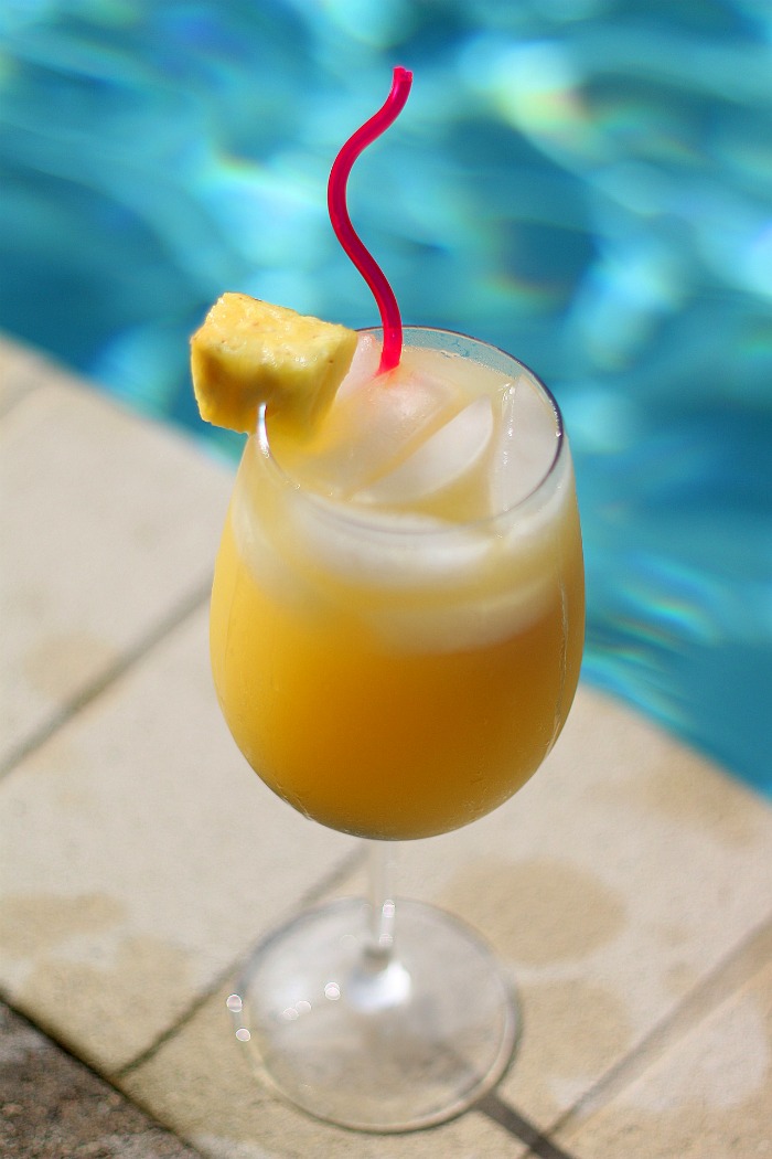 orange juice drink with a pineapple garnish near a pool Mimosa with a pineapple garnish