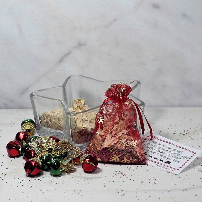 Finished magic reindeer food Red organza bag with oats and sugar near a star shaped dish and jingle bells.