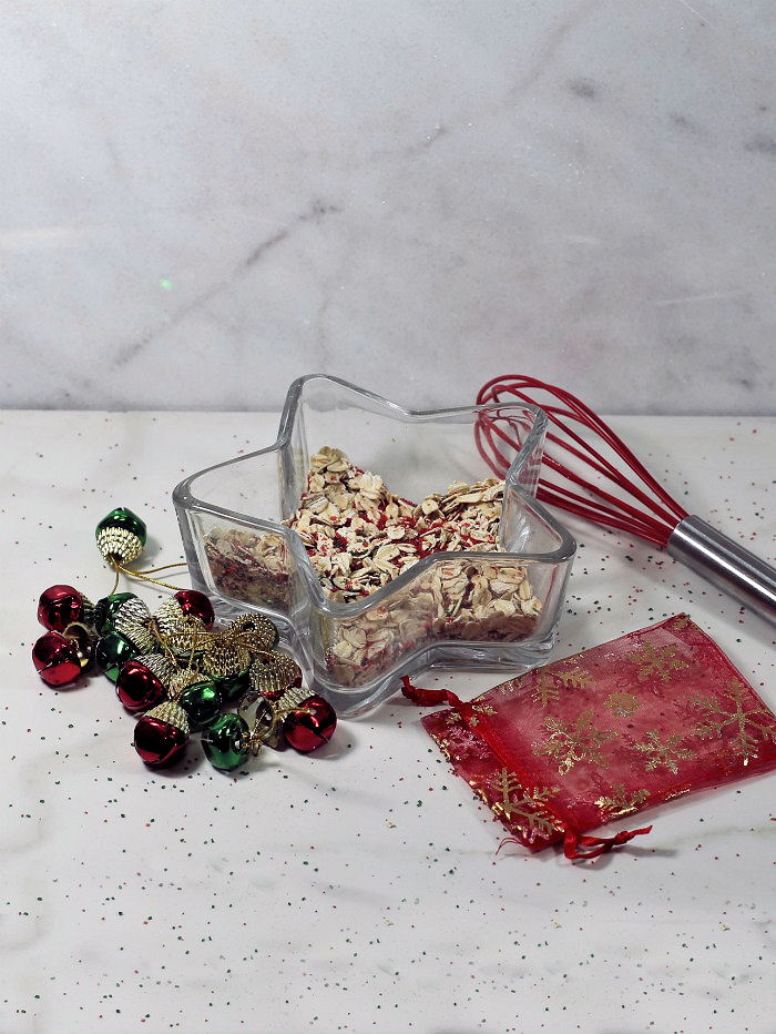 Making magic reindeer dust Rolled oats, sugar and sugar crystals in a glass star shaped bowl with whisk and red organza bag.