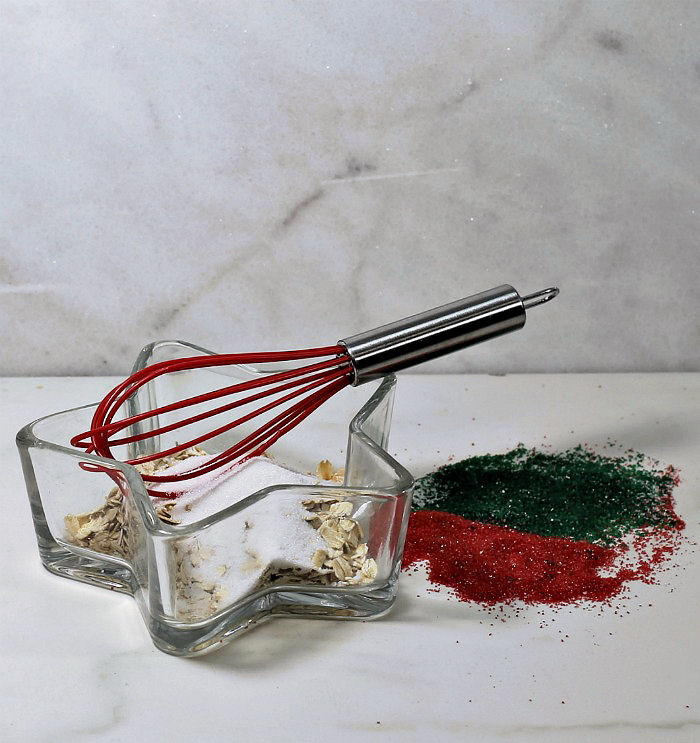 Making reindeer food. Rolled oats and sugar with whish in a star shaped bowl, with red and green sugar crystals on a counter.