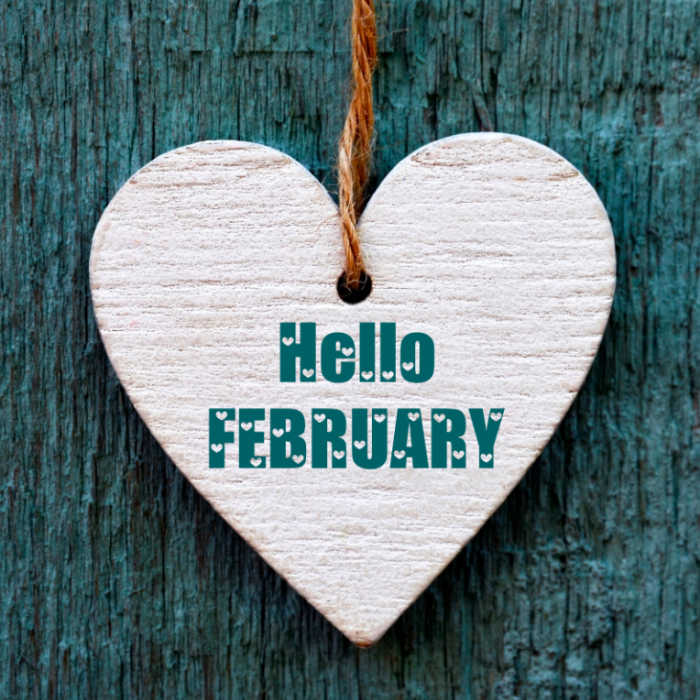 Wooden heart on a sting in front of blue wool with words "Hello February."