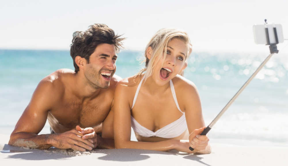 Man and woman on the beach in the water taking a selfie.
